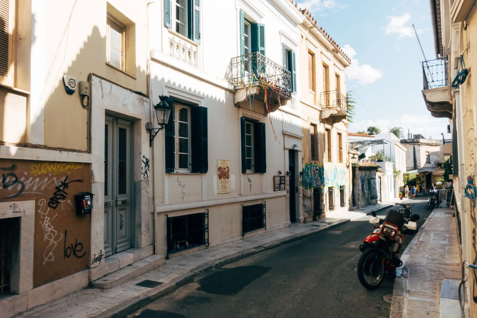 Ruelle ensoleillée du quartier de Plaka à Athènes, bordée de maisons néoclassiques aux volets verts