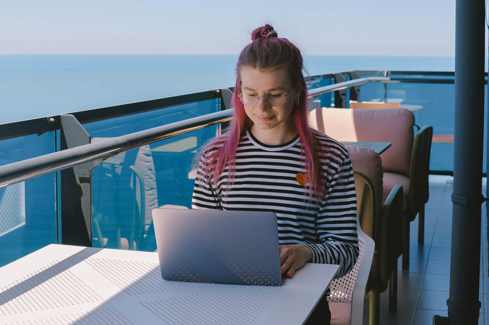 Personne travaillant sur un ordinateur portable, installée sur un balcon face à la mer