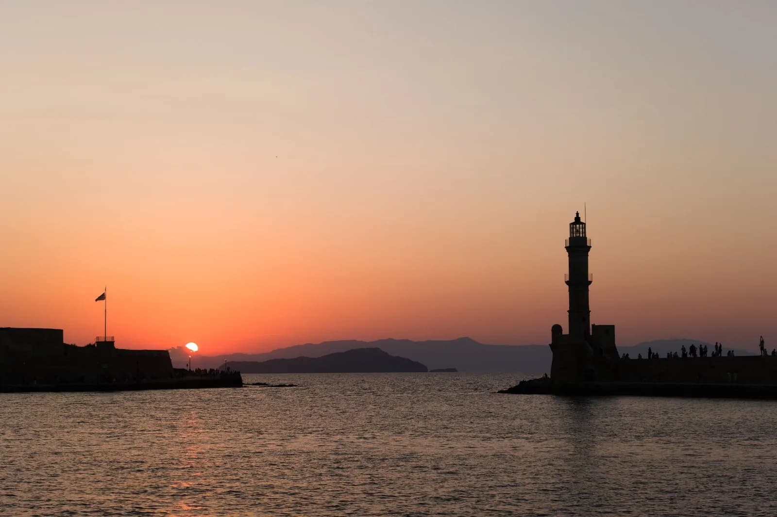 Le port vénitien de La Canée au coucher du soleil, avec le phare et les façades colorées se reflétant dans l'eau calme