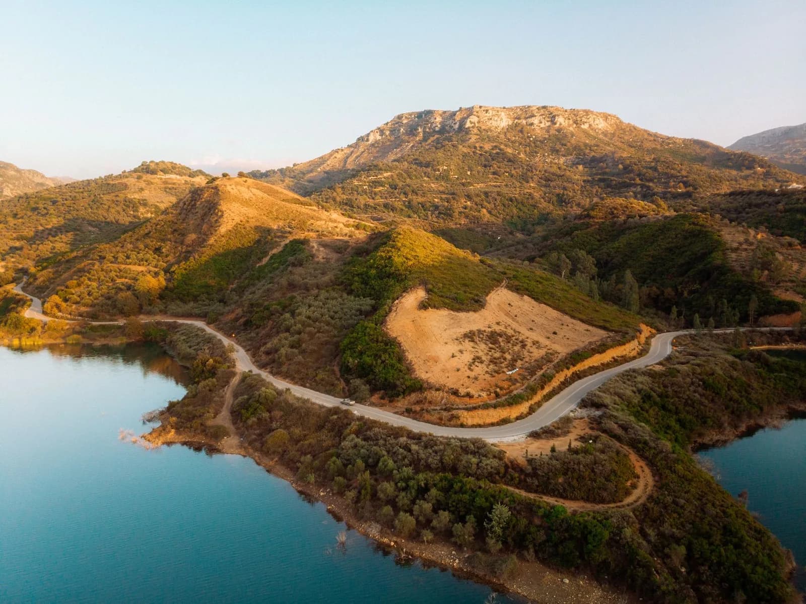Une route sinueuse longe un lac turquoise entre les collines arides de l'arrière-pays grec