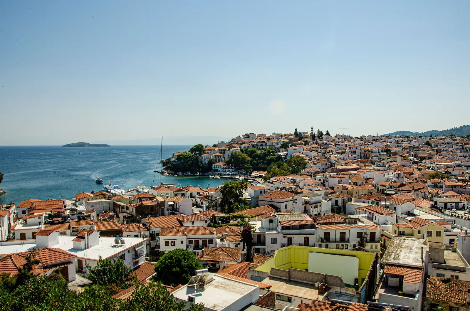Les toits de tuiles de Skiathos Ville étagés au dessus du port, avec l'îlot de Tsougria au large dans la mer Égée