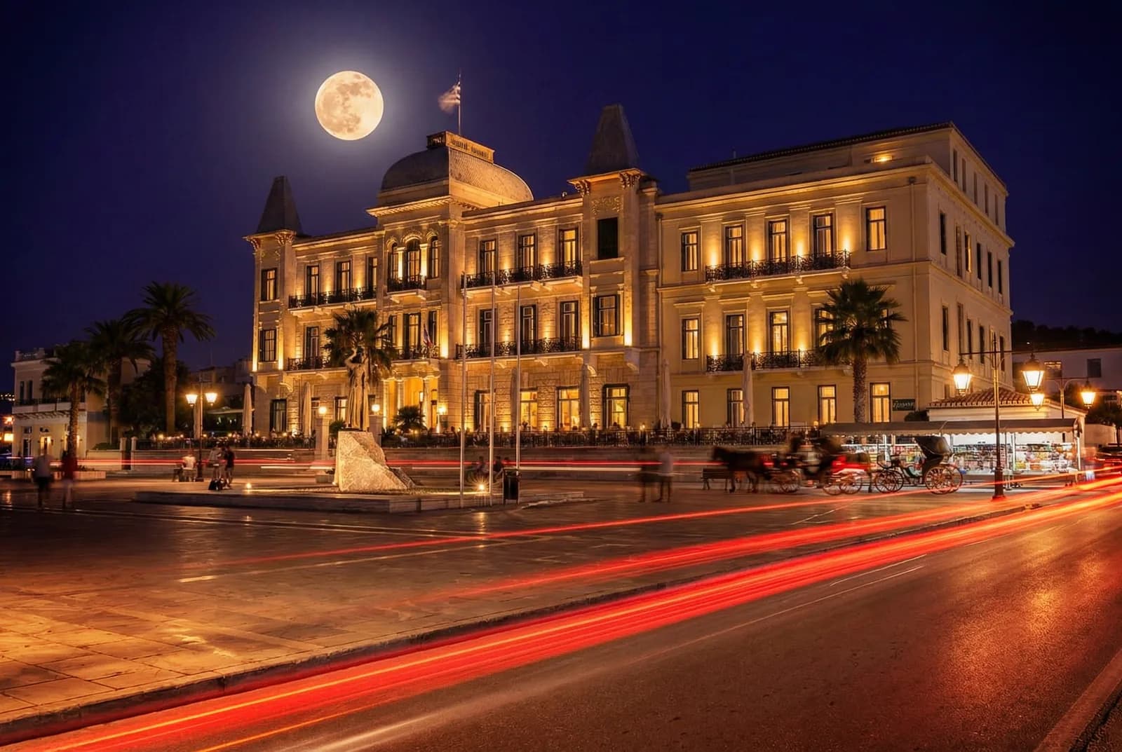 Le Poseidonion Grand Hotel illuminé de nuit sur le front de mer de Spetses, avec les calèches à l'arrêt