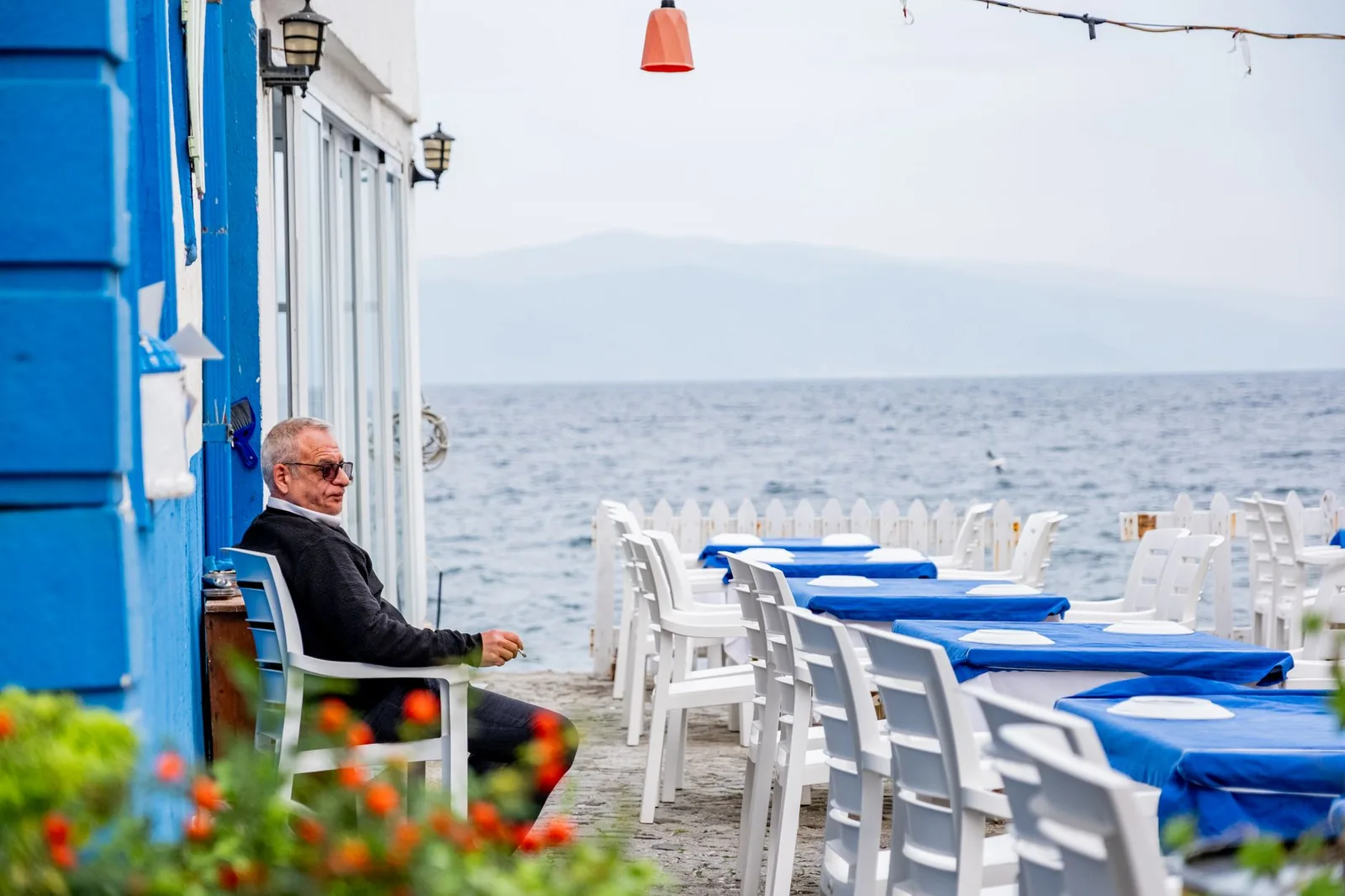 Retraité assis à la terrasse d'une taverne aux murs bleus, face à la mer