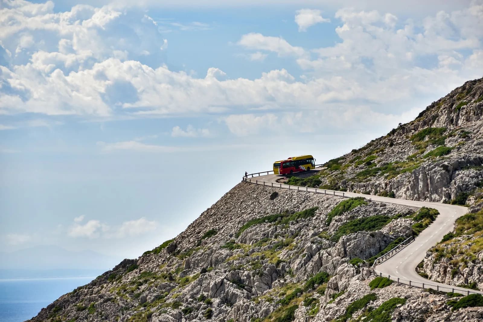 Un autocar interurbain sur une route de corniche étroite taillée dans la roche au-dessus de la mer