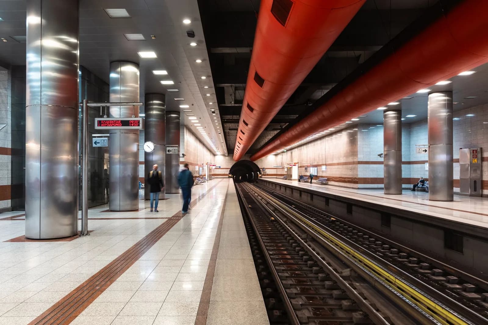 Quai du métro d'Athènes avec une rame à l'arrêt et les indications de direction en grec et en anglais