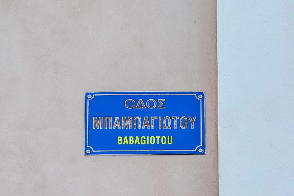Plaque de rue bleue bilingue, « ΟΔΟΣ ΜΠΑΜΠΑΓΙΩΤΟΥ » en grec et « BABAGIOTOU » en caractères latins