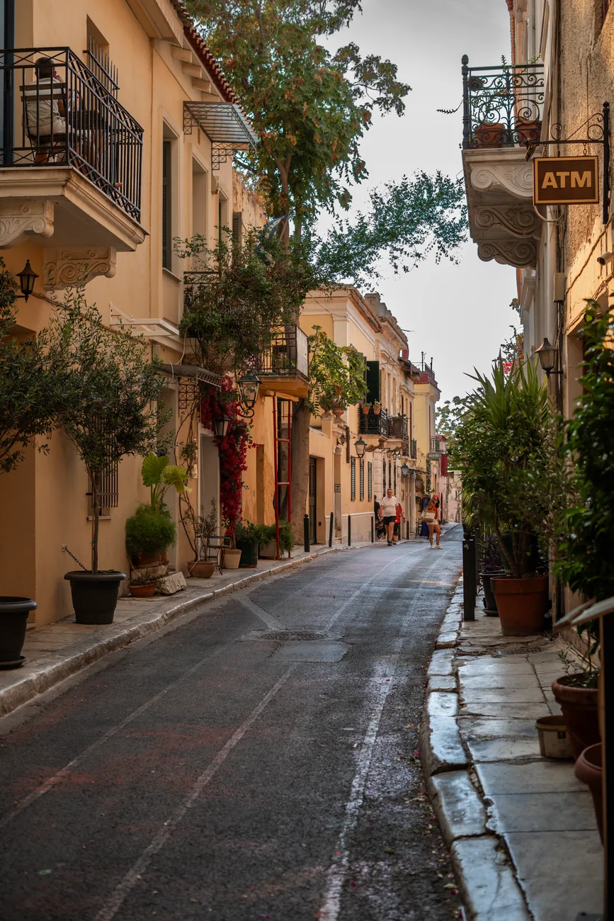 Ruelle en pente de Plaka à Athènes bordée de maisons néoclassiques ocre à balcons de fer forgé et de bougainvilliers