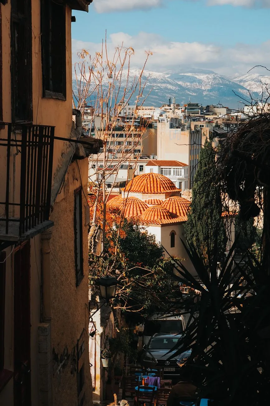 Ruelle en pente d'Athènes ouvrant sur les coupoles d'une église byzantine et les montagnes enneigées de l'Attique en hiver