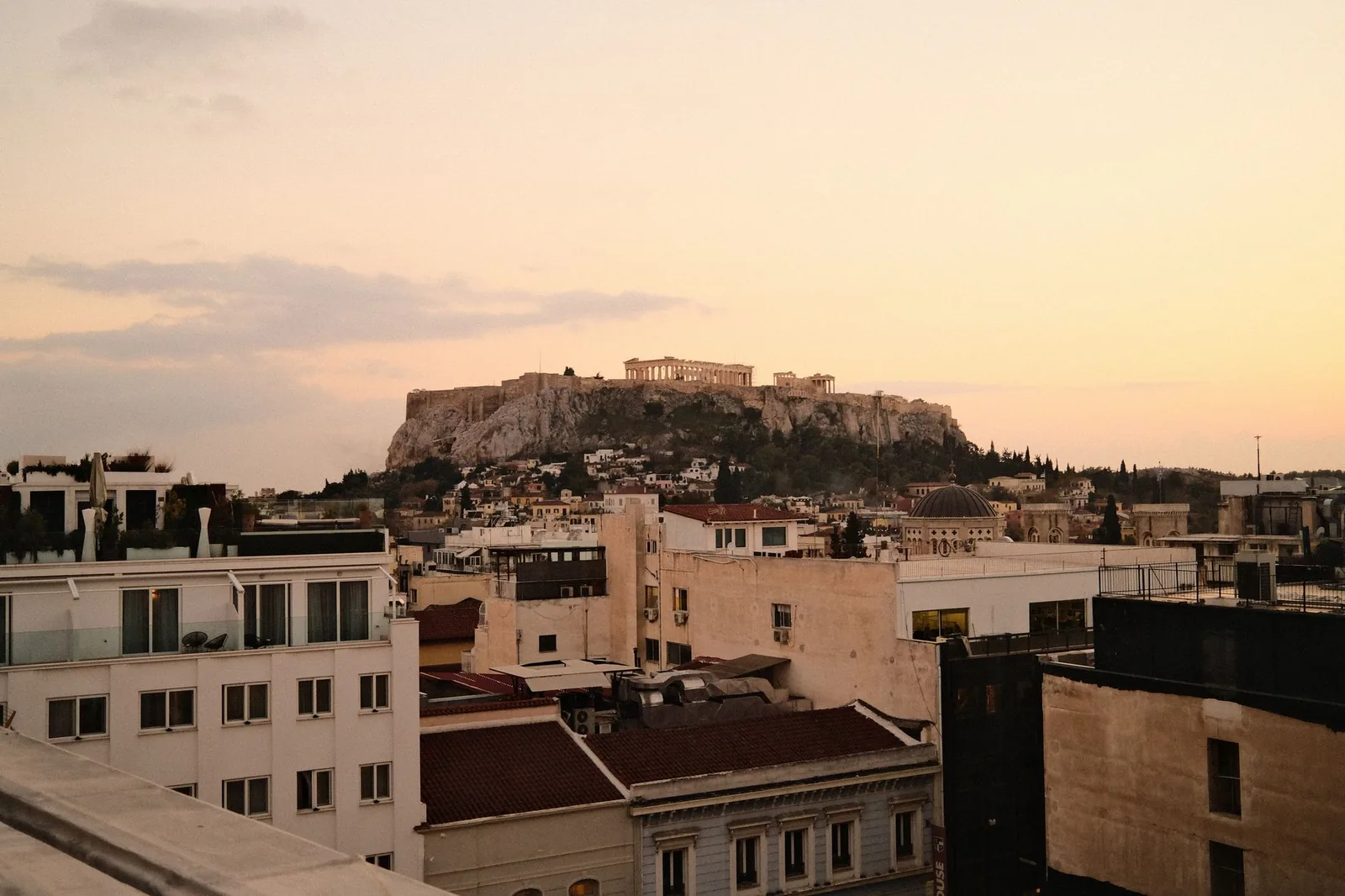 Toits-terrasses et balcons d'hôtels du centre d'Athènes face au rocher de l'Acropole et au Parthénon au coucher du soleil