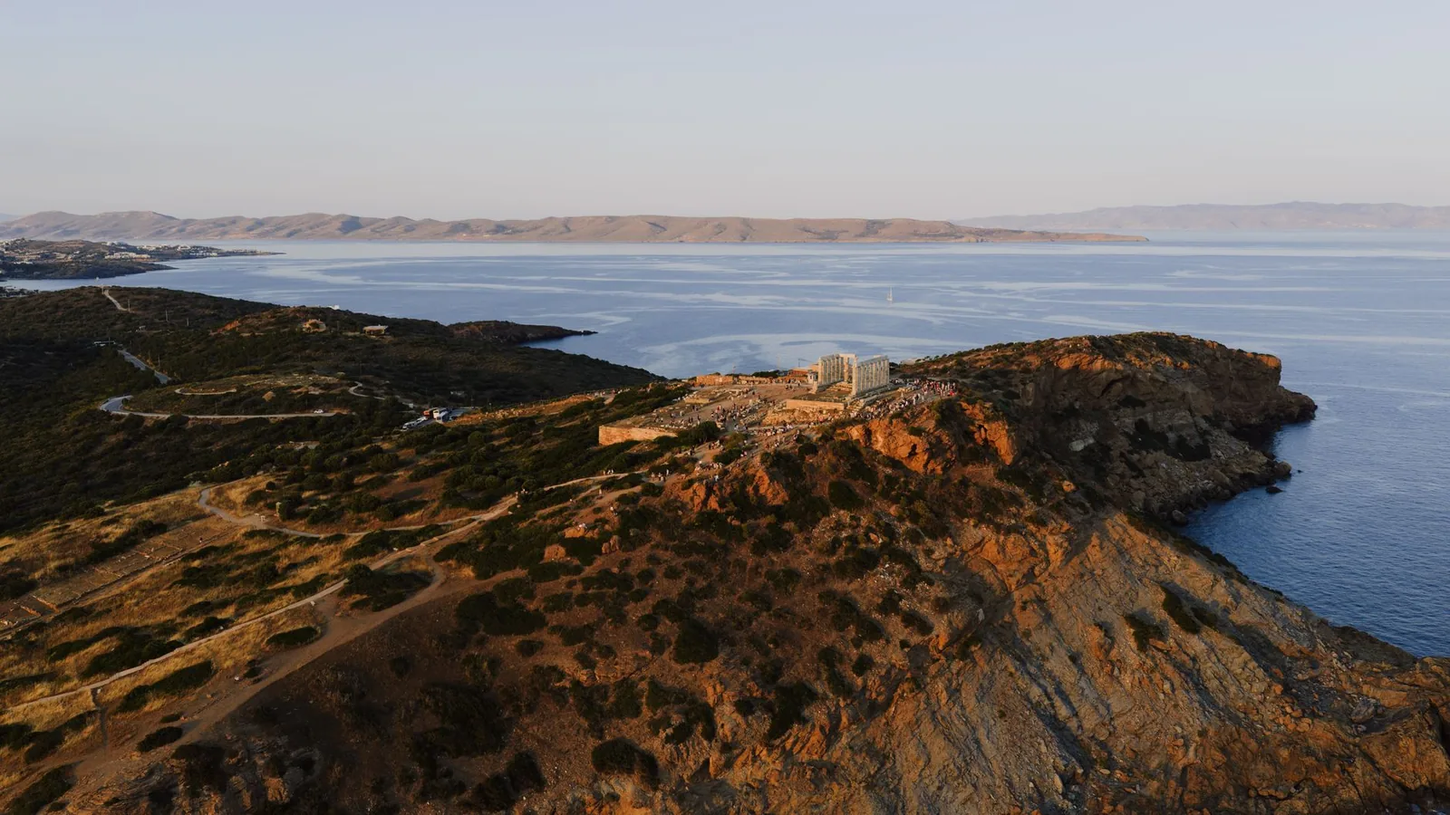 Le temple de Poséidon vu de loin sur son promontoire rocheux du cap Sounion, entouré de végétation basse