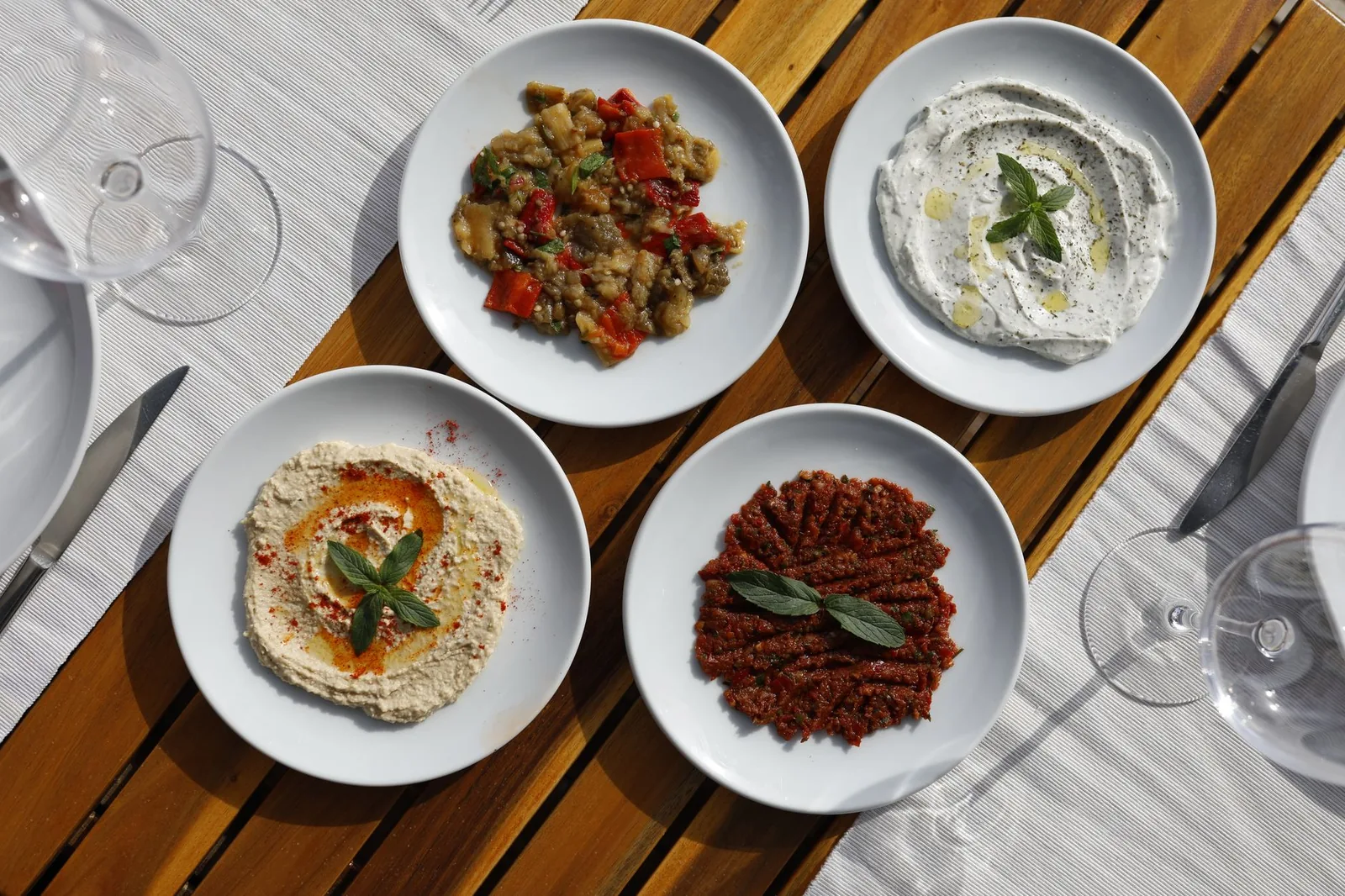 Quatre mezze grecs servis en assiettes sur une table en bois : melitzanosalata, tzatziki, fava et tirokafteri