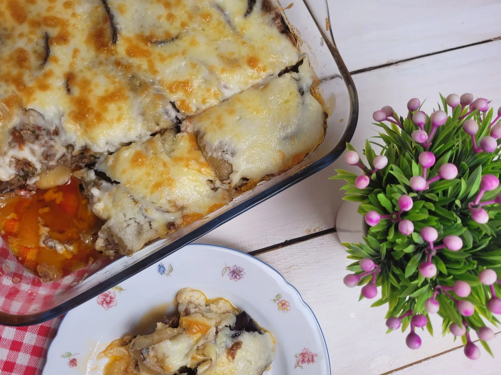 Moussaka grecque aux aubergines et à la béchamel gratinée, servie dans son plat à four avec une part dans une assiette