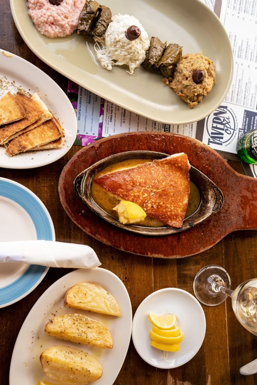 Table de taverne grecque avec un saganaki dans sa poêle, un plateau de mezze, du pain pita et la carte posée à côté