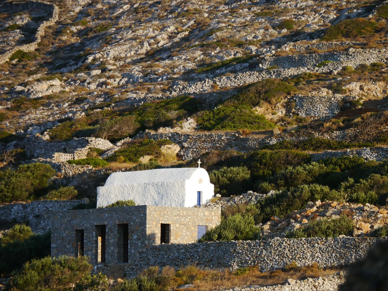 Chapelle blanche isolée sur un flanc de colline aride bordé de murets de pierre sèche, paysage de l'intérieur d'Égine