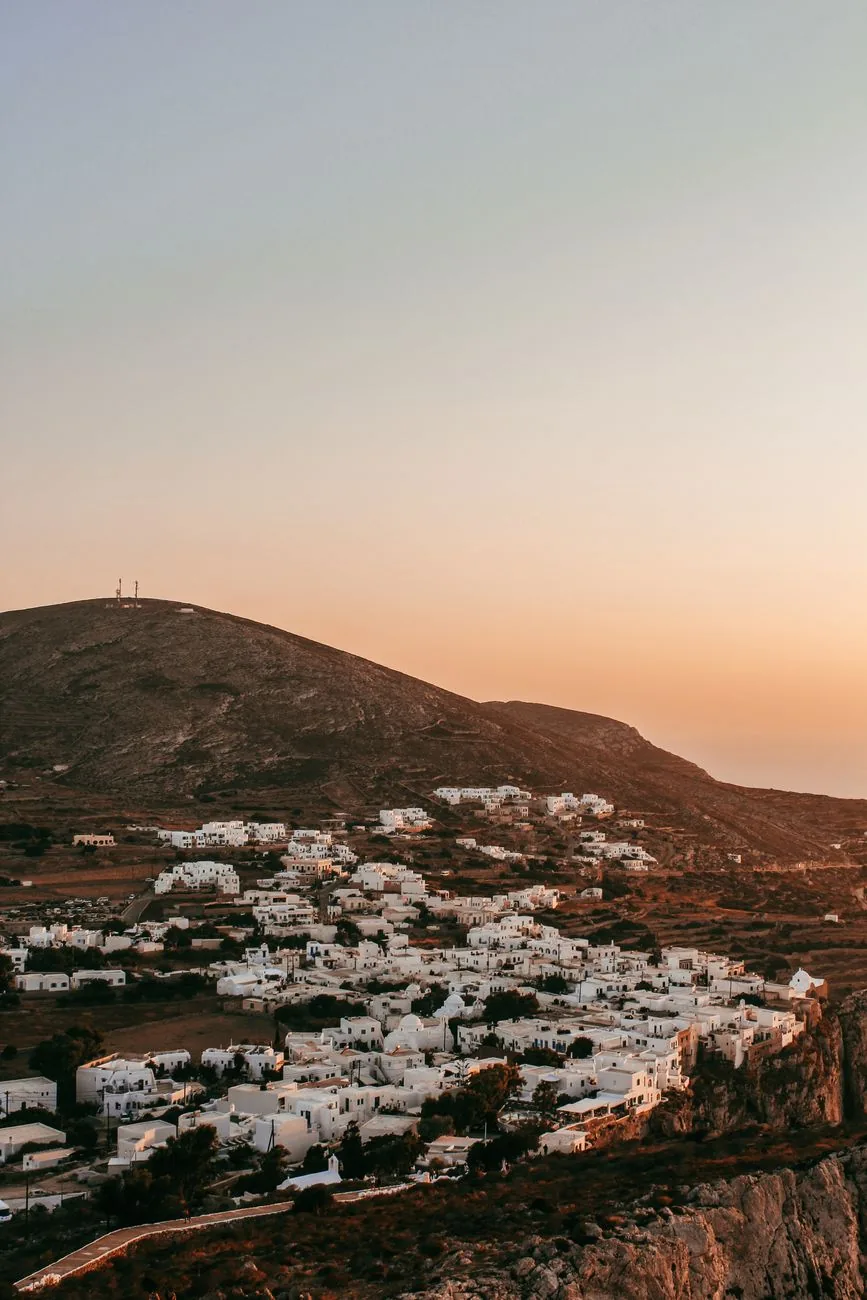 Le village blanc de la Chora de Folegandros au coucher du soleil, étalé sur le plateau au-dessus de la falaise qui tombe dans la mer Égée