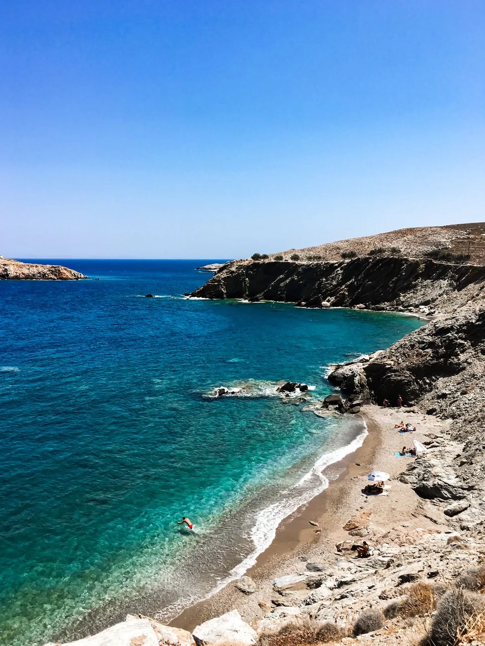 Crique de galets de Folegandros bordée de falaises arides, avec une eau turquoise qui vire au bleu profond au large