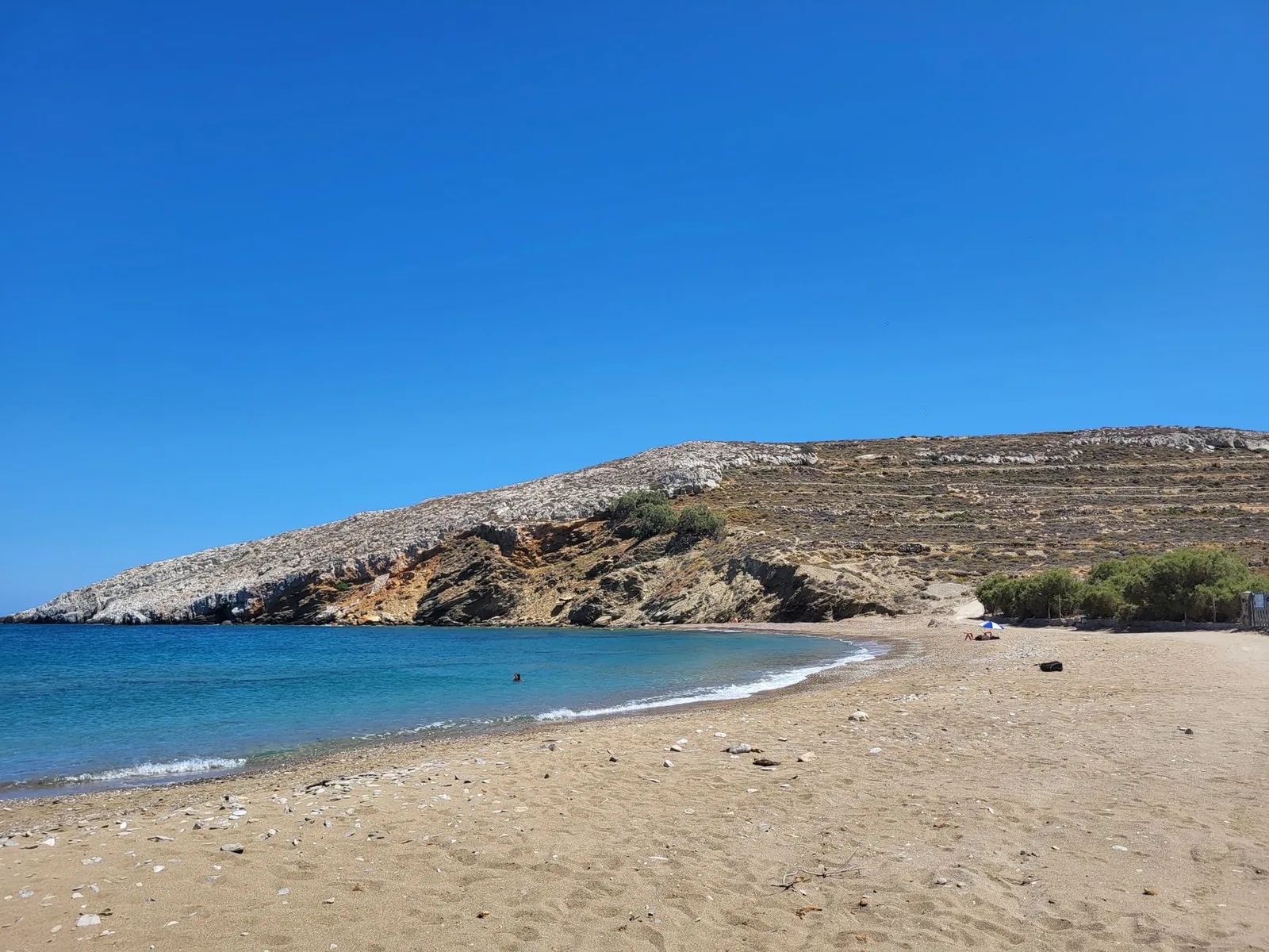 Grande plage de sable clair de Folegandros au pied de collines arides en terrasses, avec une eau bleue peu profonde