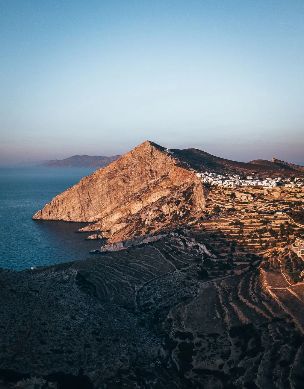 Le rocher de la Panagia dominant la Chora de Folegandros à la lumière du couchant, avec l'église blanche visible tout en haut et les terrasses en pierre sèche au premier plan