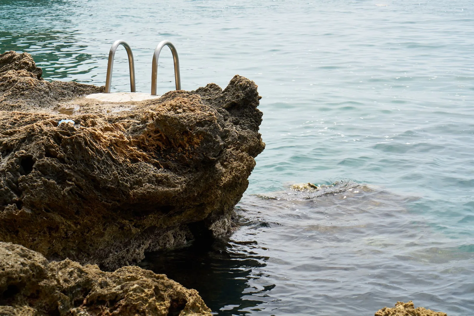 Rochers plats équipés d'une échelle métallique donnant sur une eau profonde et limpide, mode de baignade typique d'Hydra