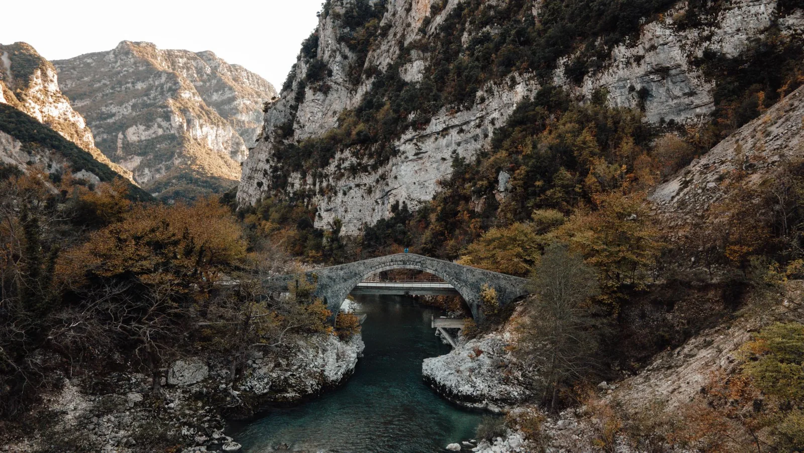 Pont de pierre à une arche au-dessus d'une rivière turquoise dans une gorge boisée de l'Épire