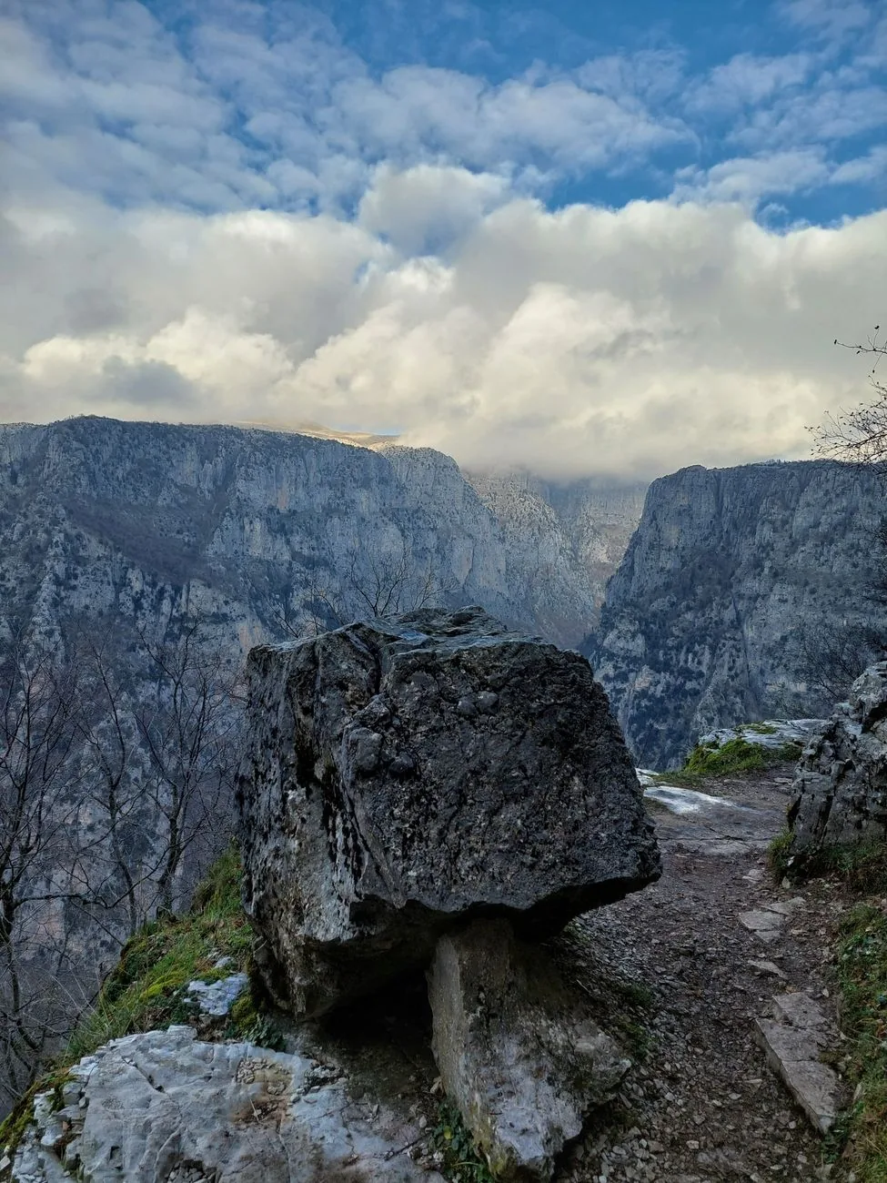 Gros rocher au bord d'un sentier dominant les falaises des gorges de Vikos, sous un ciel nuageux