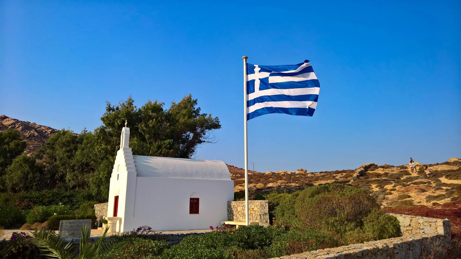 Petite chapelle blanche et drapeau grec sur les collines arides du nord d'Ios, face à la mer