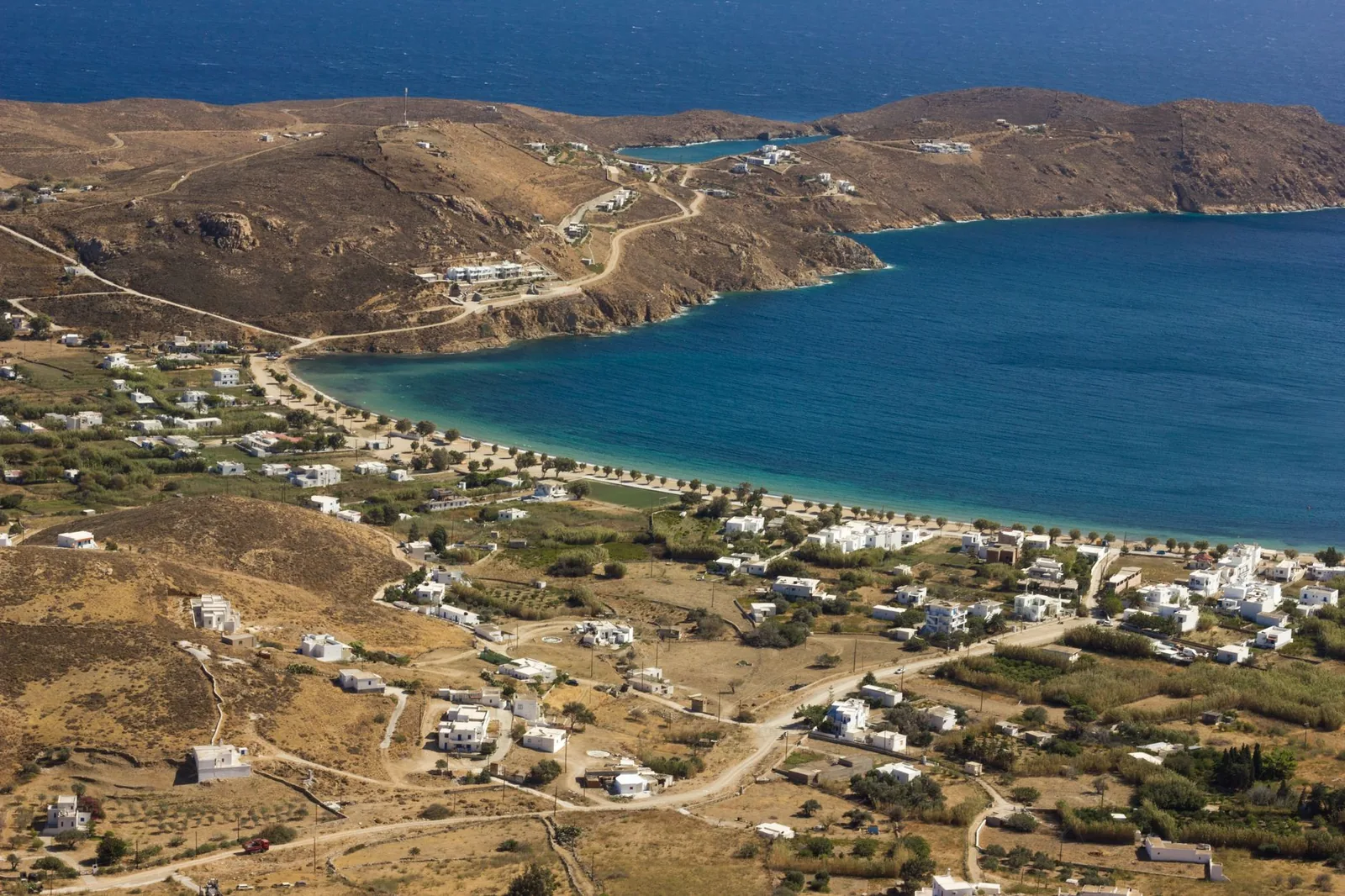 Grande baie de sable blond bordée d'hôtels blancs et de collines arides, la plage de Mylopotas à Ios