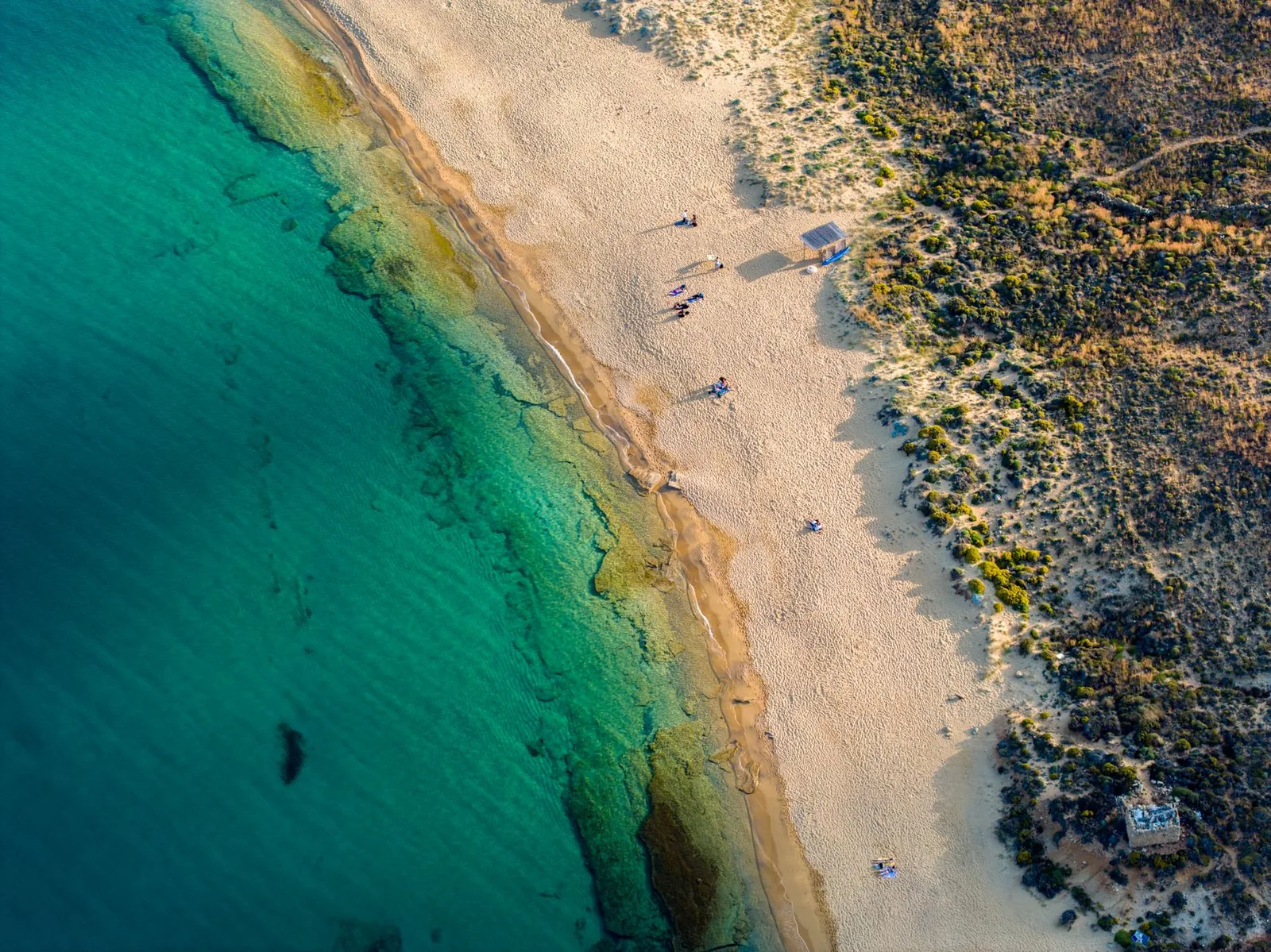 Longue plage de sable déserte bordée d'eau turquoise et de collines sèches, sur la côte est d'Ios