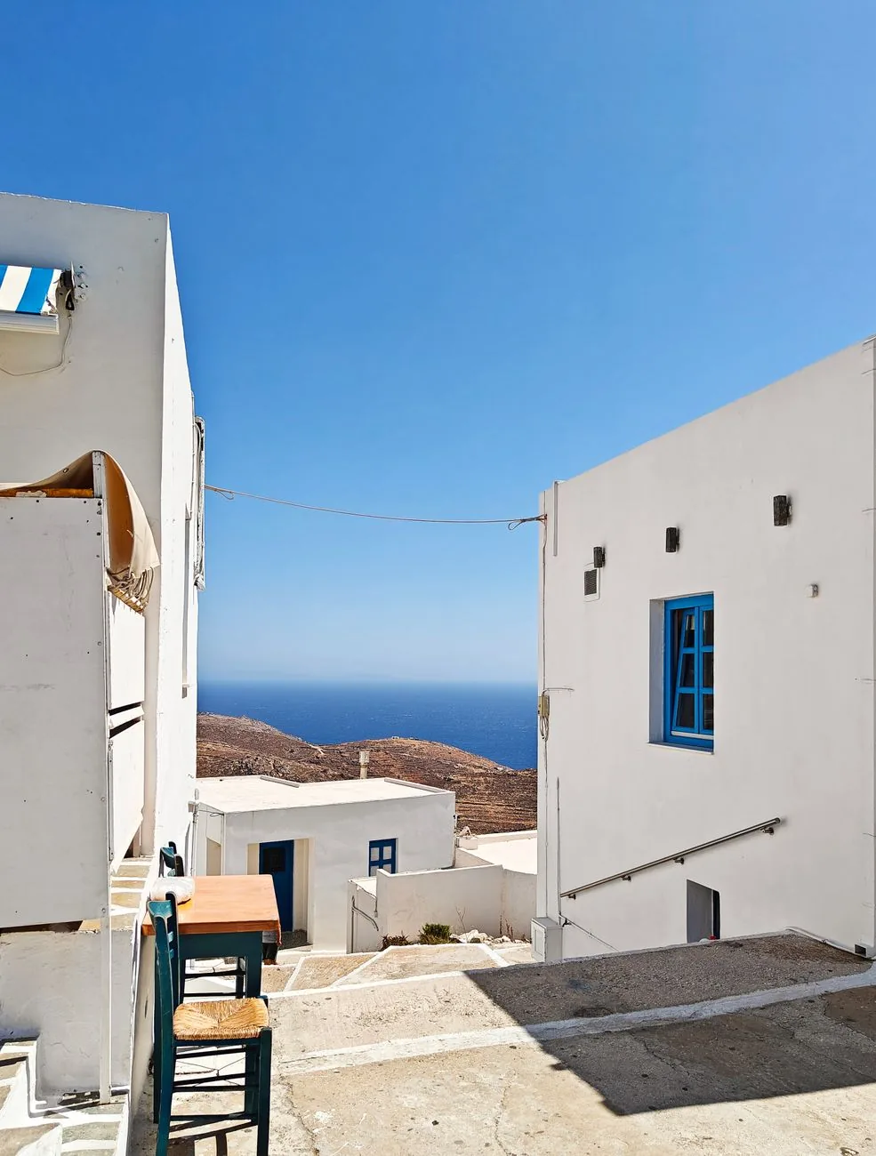 Terrasse de taverne entre les maisons blanches d'un village cycladique dominant la mer Égée, à Ios