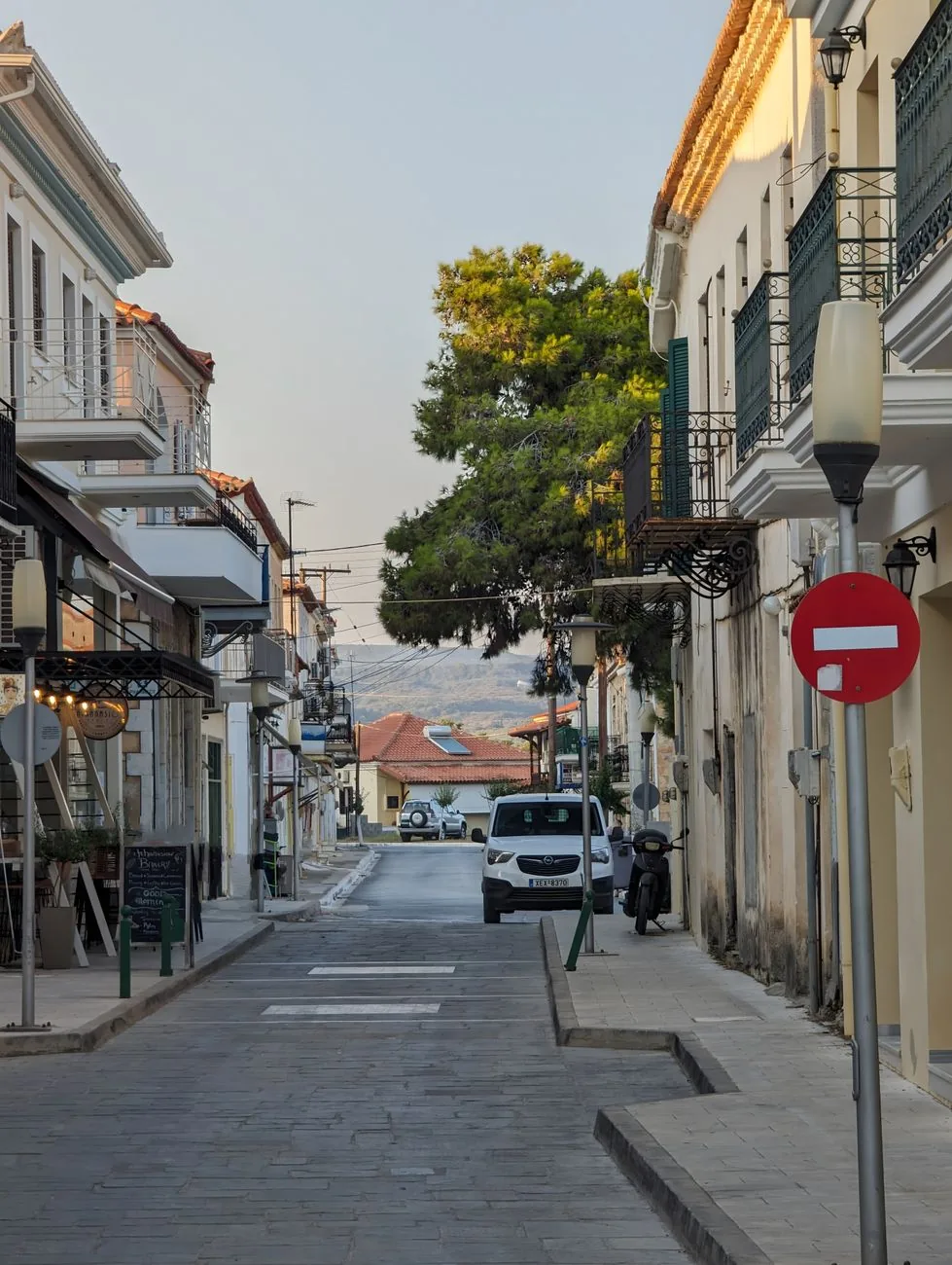 Ruelle piétonne du centre-ville en Grèce continentale, bordée de terrasses de cafés et de balcons néoclassiques, avec les montagnes en arrière-plan, ambiance du centre historique de Kalamata