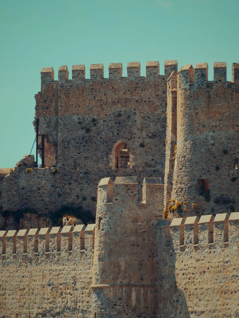 Remparts crénelés et tour en ruine d'un château médiéval en pierre, évoquant le château franc de Villehardouin qui domine Kalamata