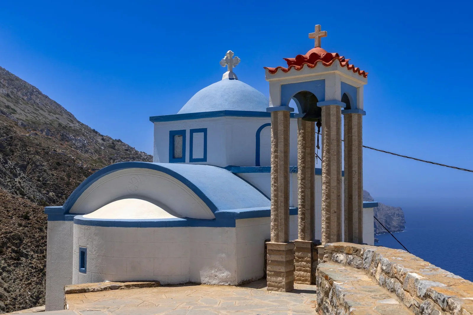 Chapelle à coupole bleue et clocher à tuiles rouges posée sur une falaise de Karpathos, au dessus de la mer Égée