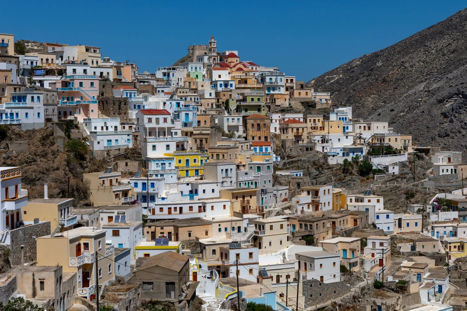 Les maisons colorées d'Olympos étagées à flanc de crête à Karpathos, avec le moulin à vent et le clocher au sommet