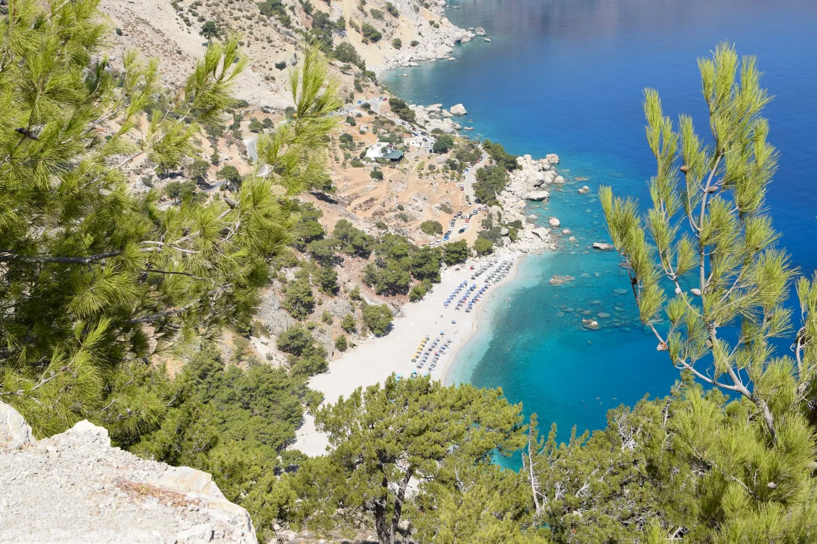 Anse de la côte est de Karpathos vue à travers les pins, sa plage de sable clair et son eau qui passe du turquoise au bleu profond