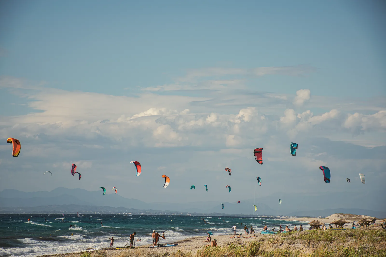 Plage de spot de kitesurf en Grèce, une vingtaine d'ailes en vol au dessus de la mer et le matériel posé sur le sable