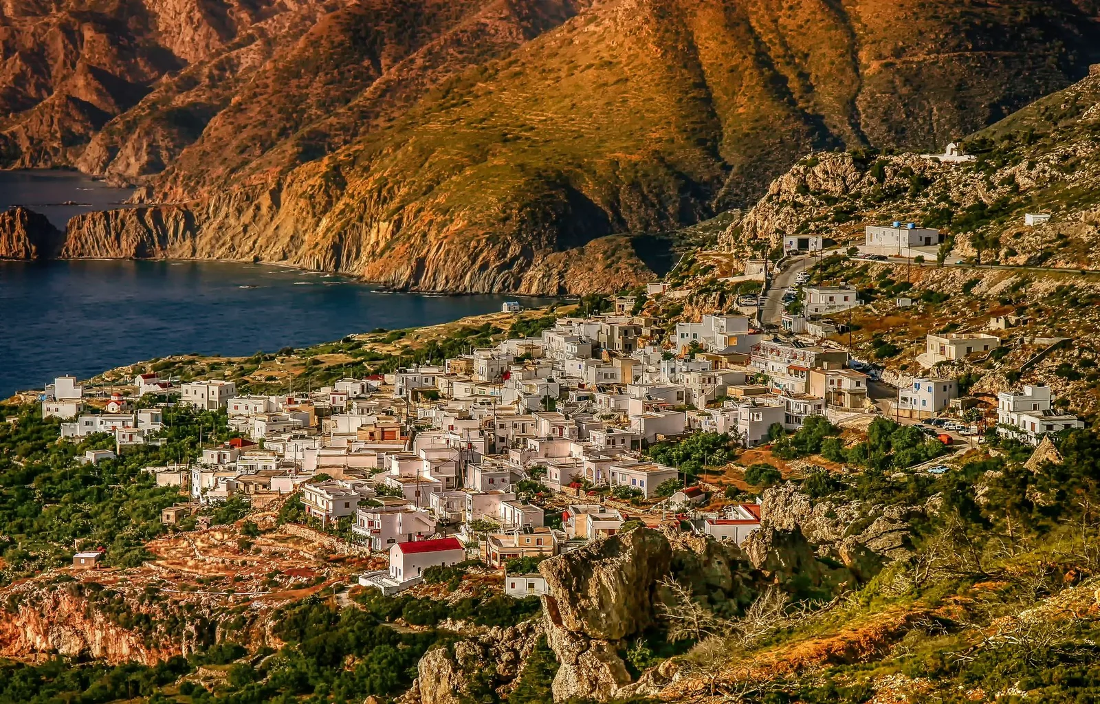 Village blanc de Karpathos accroché au dessus de la côte ouest dans la lumière dorée du soir, adossé à un versant montagneux