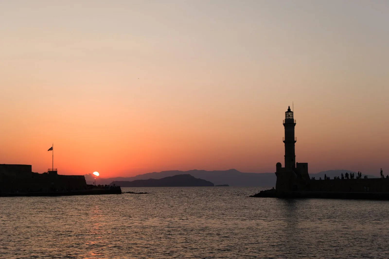 Le vieux port vénitien de La Canée au coucher du soleil, avec le phare égyptien au bout de la jetée et les façades colorées des anciennes maisons vénitiennes se reflétant dans l'eau calme