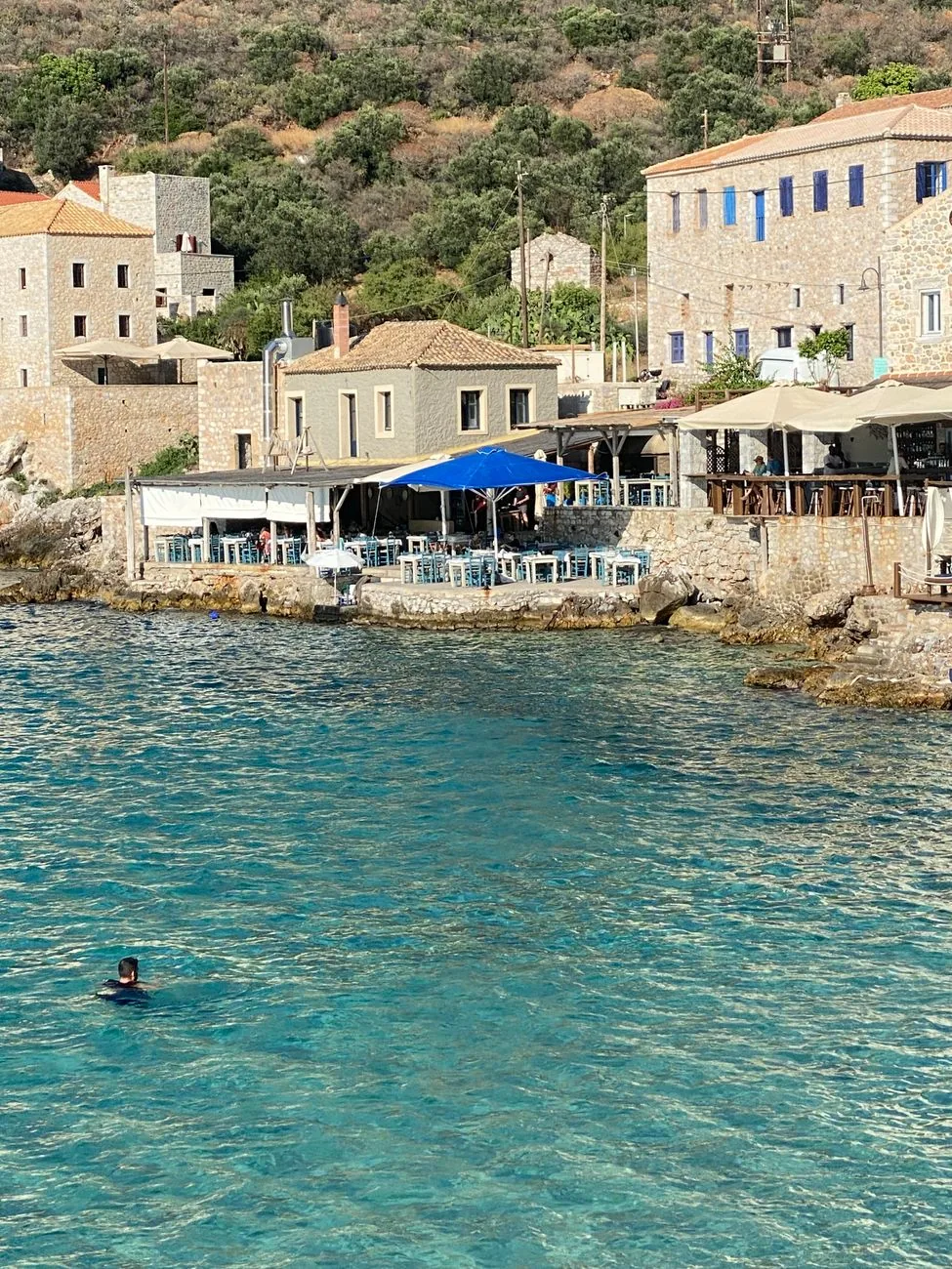 Tavernes et terrasses bleues au ras de l'eau turquoise du port de Limeni, dans le Magne, avec des maisons-tours en pierre au dessus