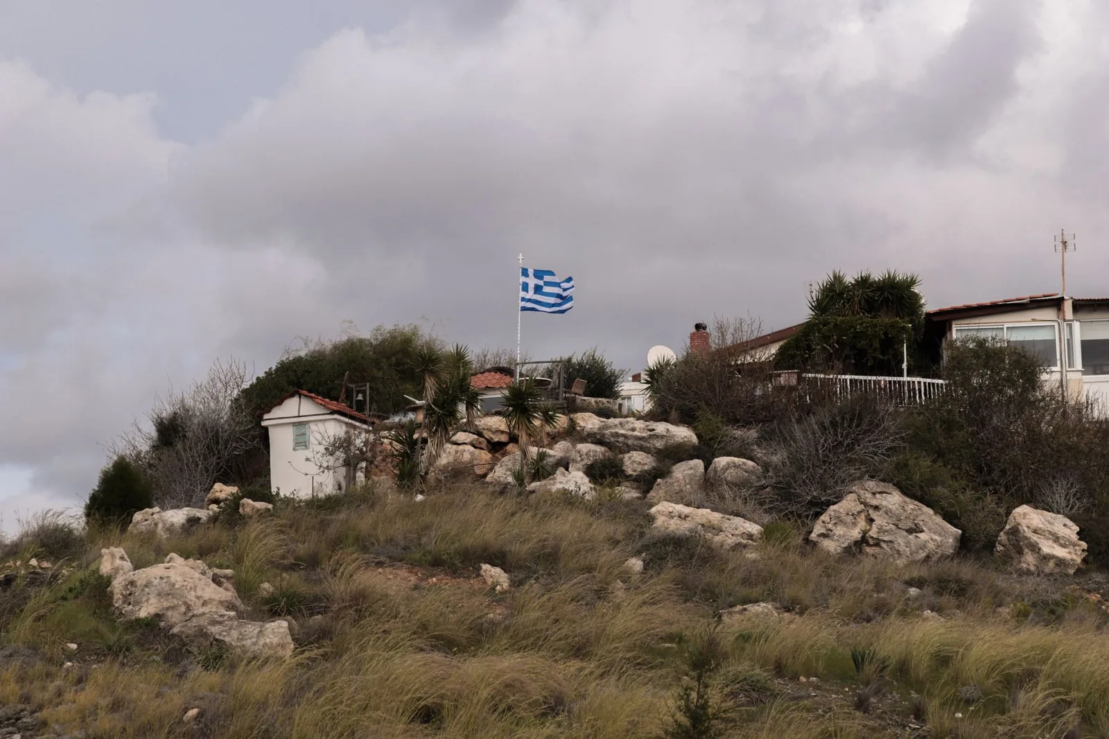Drapeau grec battu par le vent sous un ciel gris et bas, sur une colline en hiver