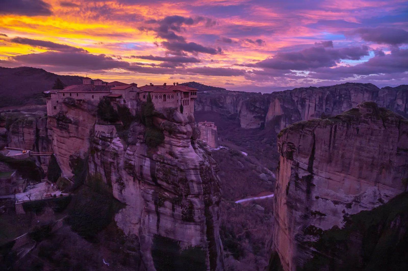 Les monastères de Varlaam et du Grand Météore éclairés par un ciel violet et orange au crépuscule, aux Météores