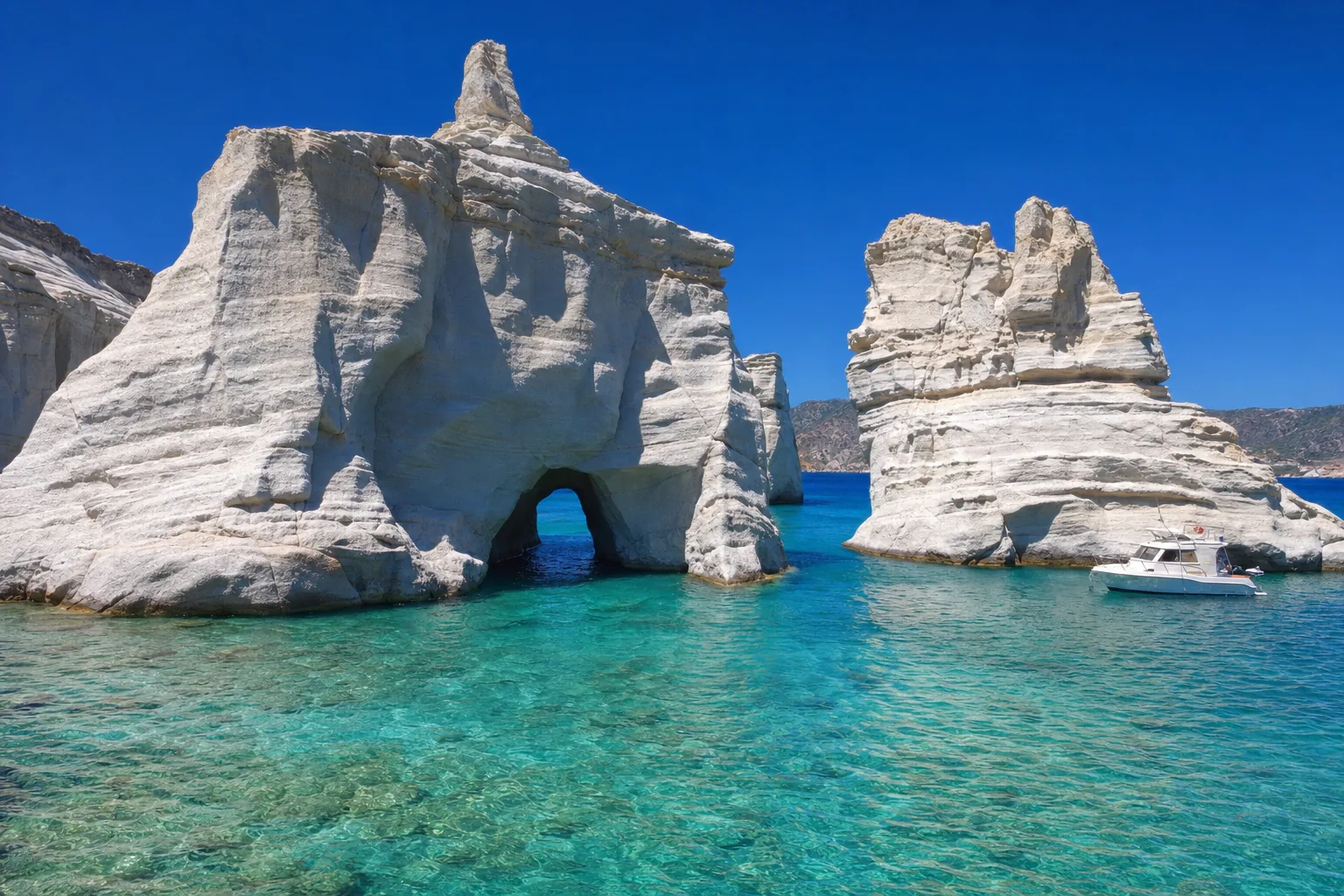 Les arches et pitons de roche blanche de Kleftiko émergeant d'une eau turquoise à Milos, avec un bateau au mouillage au pied des falaises