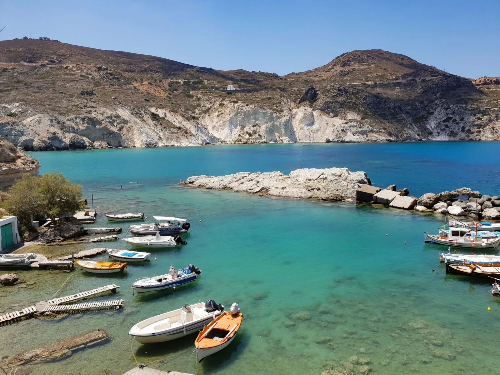 Barques de pêche amarrées dans une crique aux eaux turquoise de Milos, au pied de collines arides et de falaises blanches