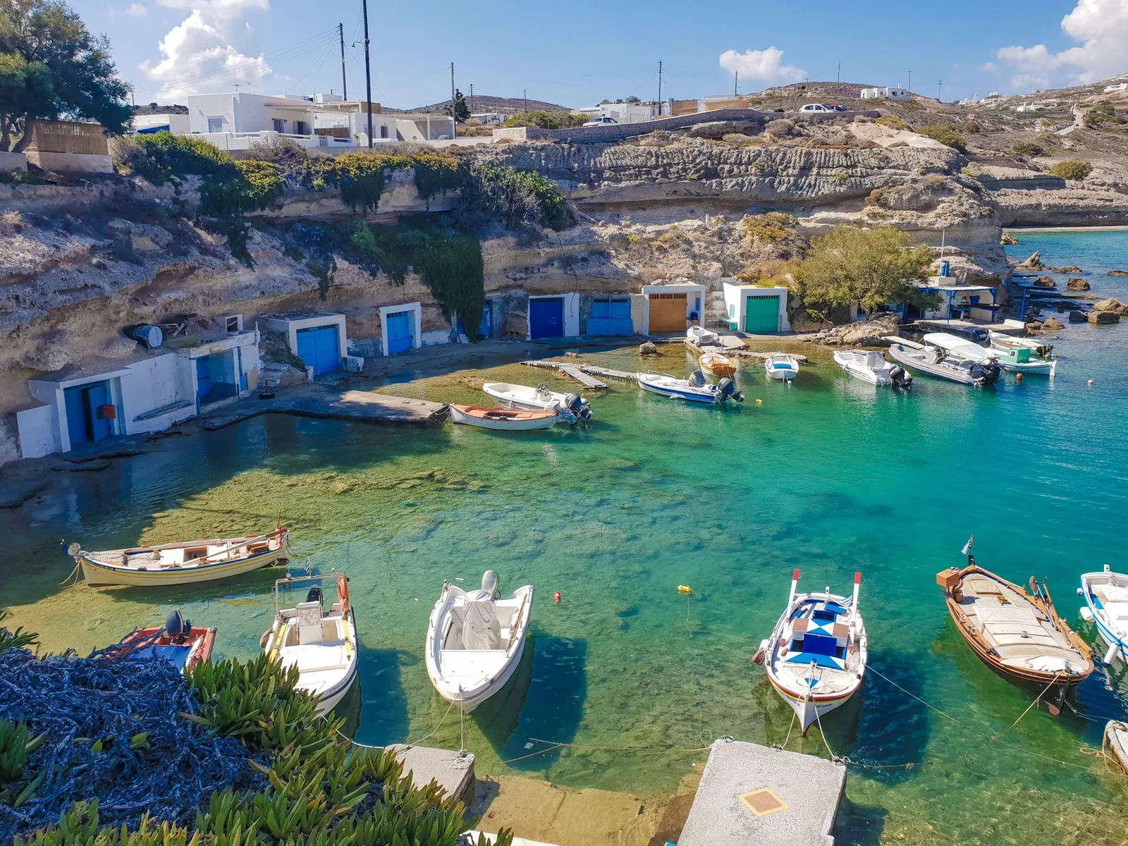 Syrmata aux portes bleues et turquoise creusés dans la falaise et barques amarrées dans le petit port de pêche de Mandrakia, sur la côte nord de Milos
