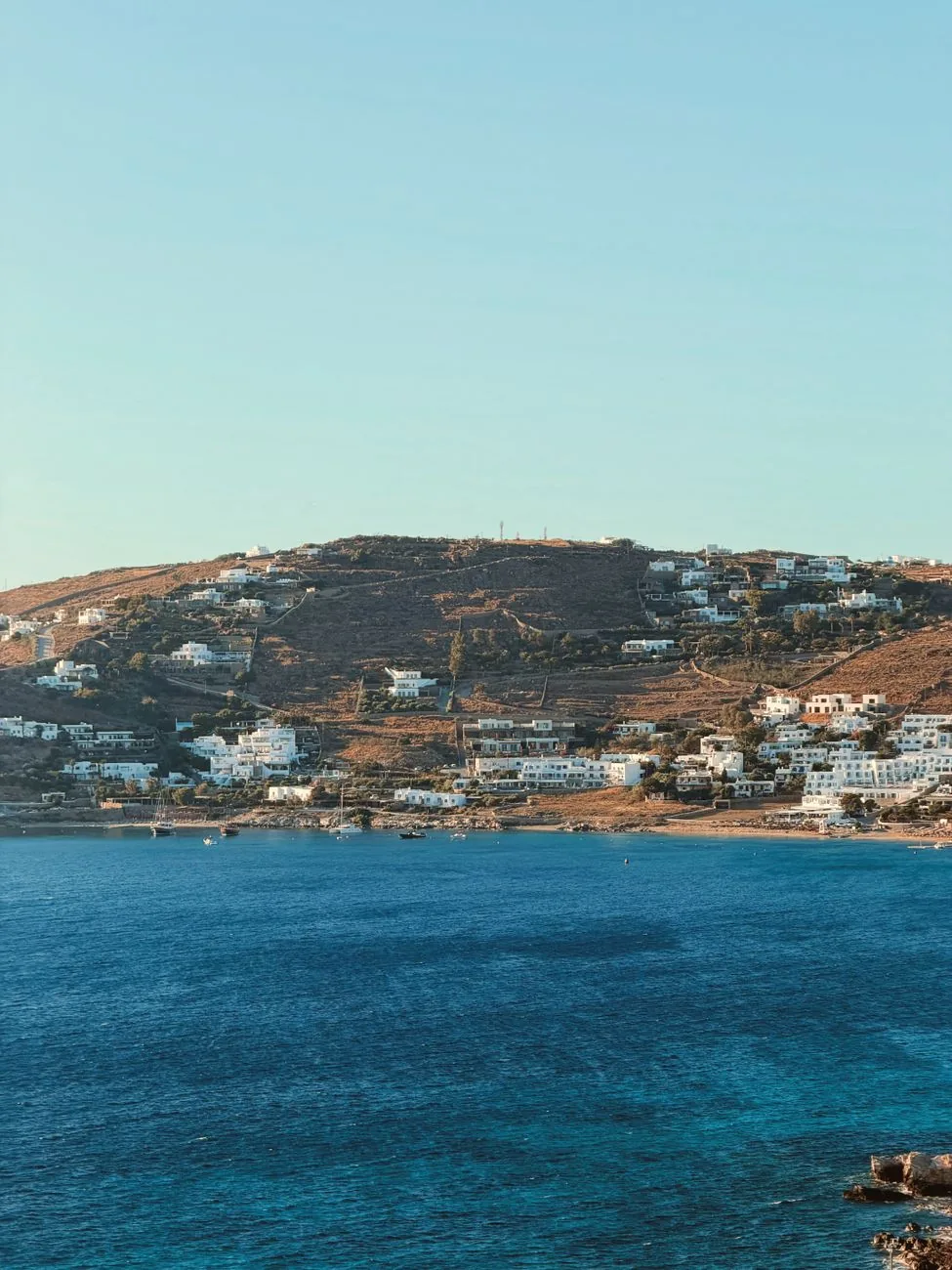 Baie calme de Mykonos bordée de maisons blanches descendant vers une mer turquoise