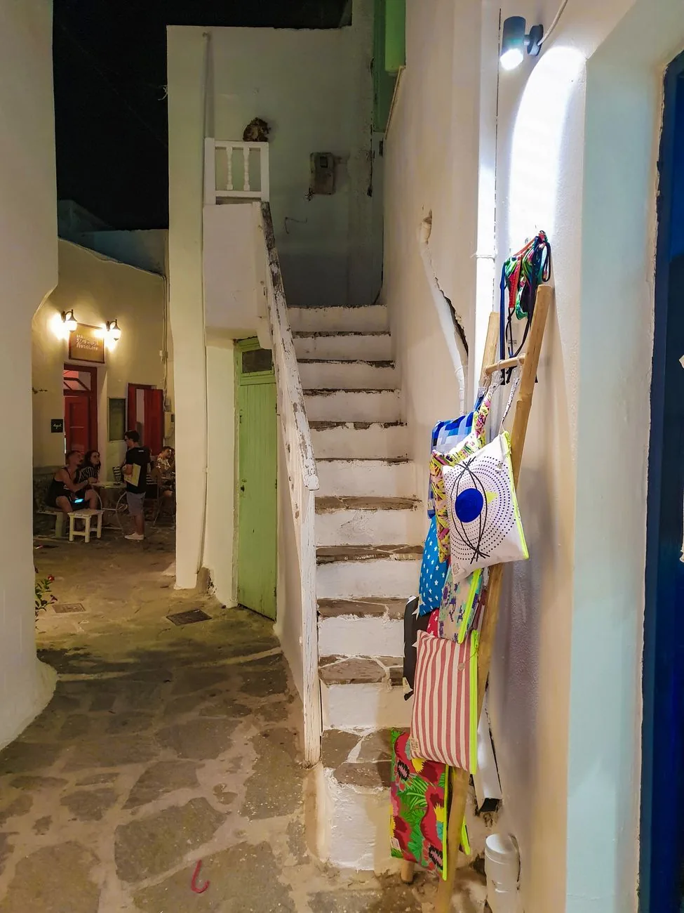 Ruelle de Chora à Mykonos illuminée la nuit, avec une taverne et des boutiques ouvertes