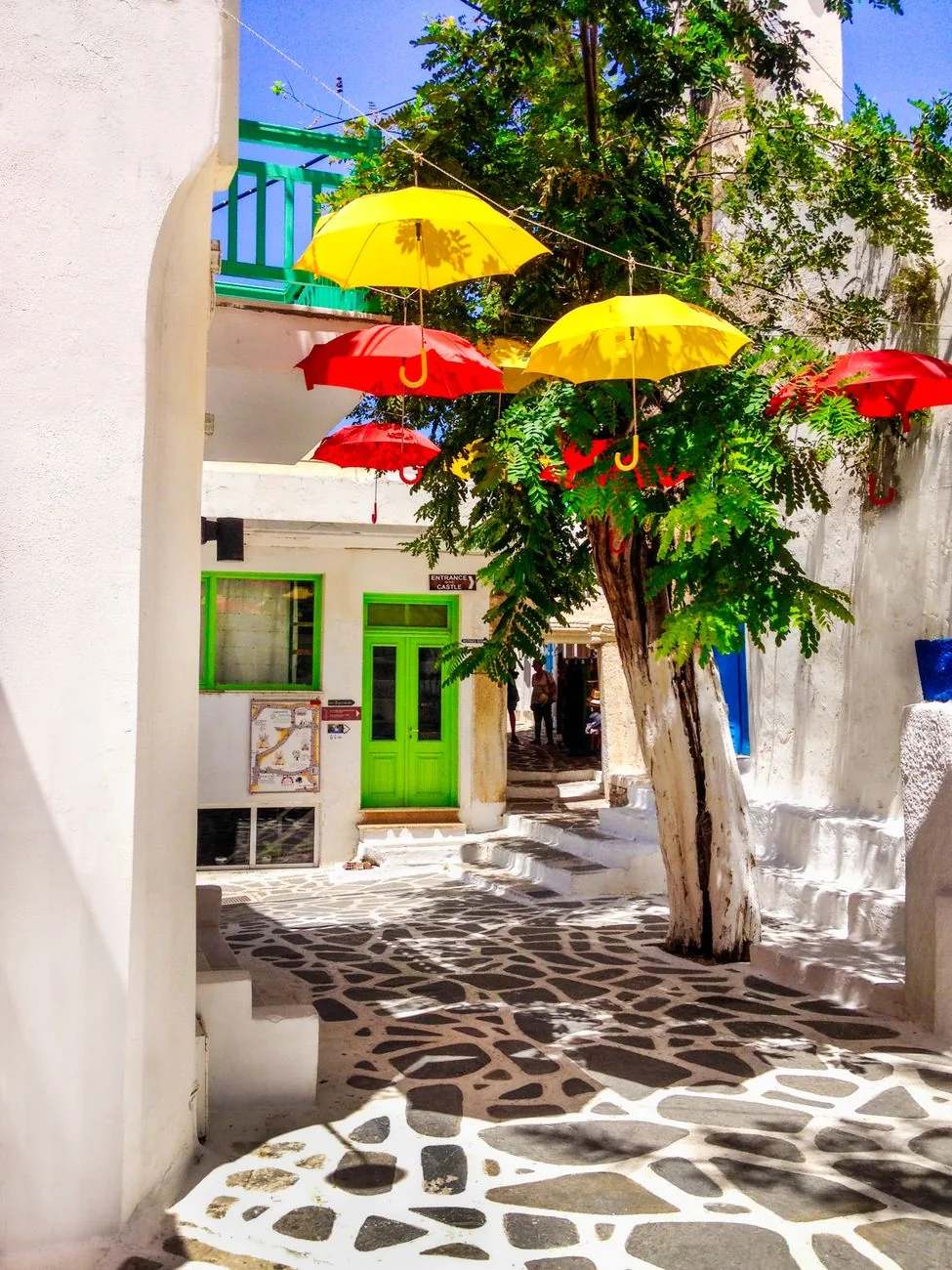 Ruelle blanche pavée de Chora à Mykonos, décorée de parasols colorés suspendus