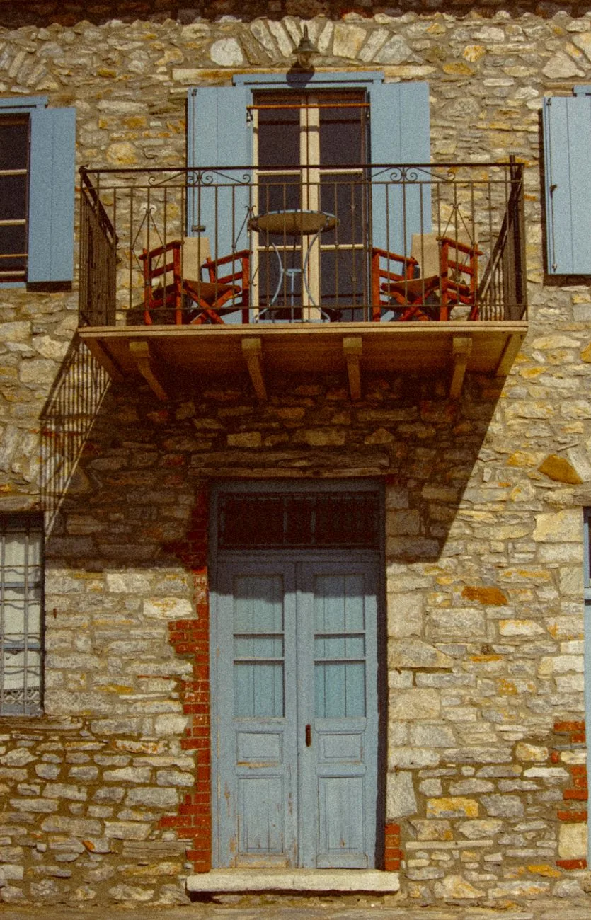 Façade d'un archontiko du Pélion, ses murs de pierre, son balcon de bois en encorbellement et ses volets bleu pâle