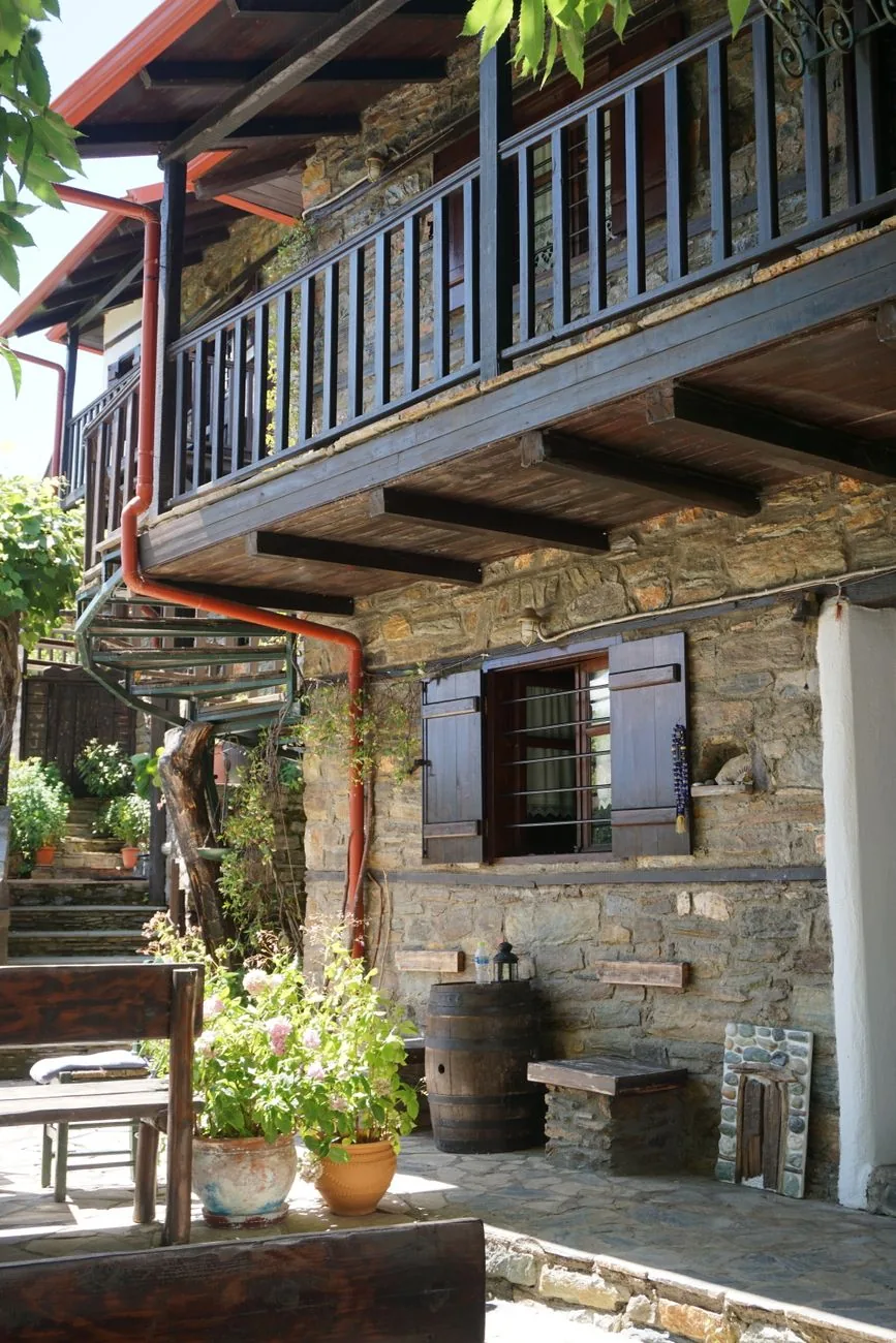 Maison d'hôtes traditionnelle en pierre de schiste dans un village du Pélion, sa galerie de bois et sa terrasse dallée