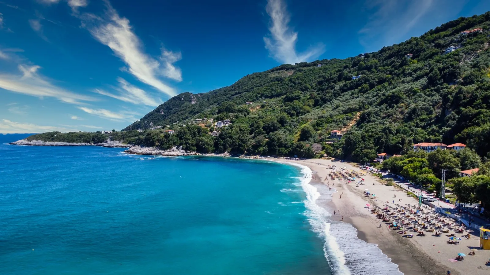 Longue plage de sable d'Agios Ioannis dans le Pélion, ses parasols et les collines boisées qui plongent dans la mer Égée