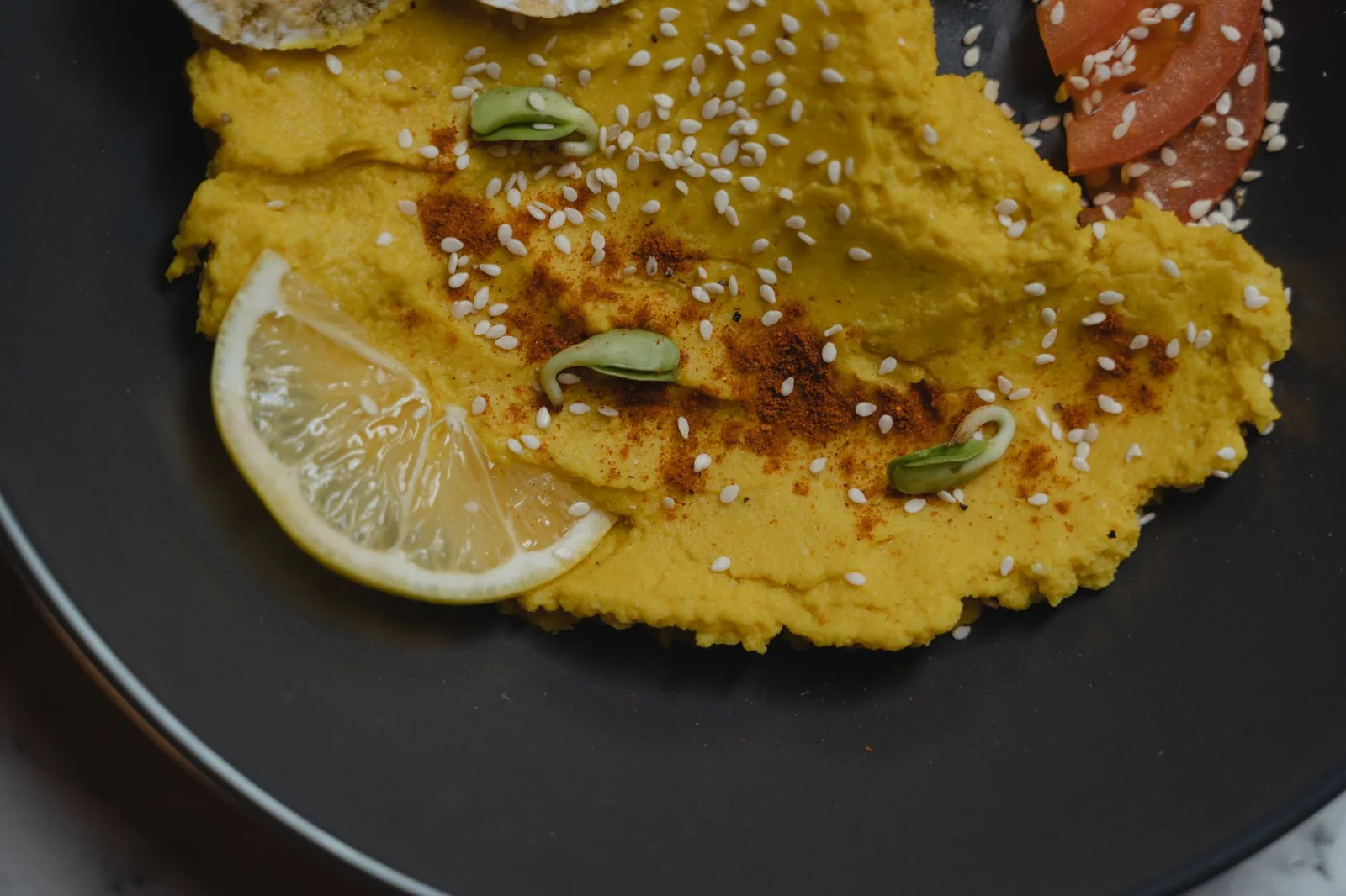 Fava grecque, purée jaune de pois cassés étalée dans une assiette sombre, saupoudrée de paprika et de graines de sésame, avec une rondelle de citron
